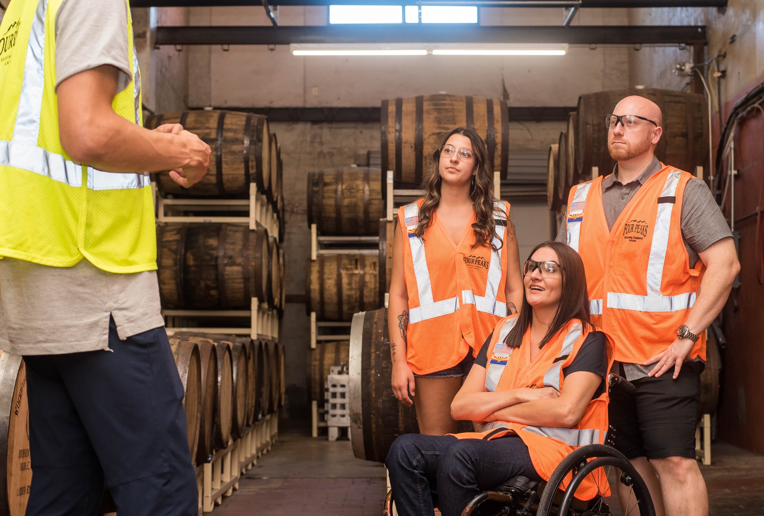Tres trabajadores (una de las cuales está en silla de ruedas) con chalecos reflectantes en una bodega, recibiendo instrucciones.